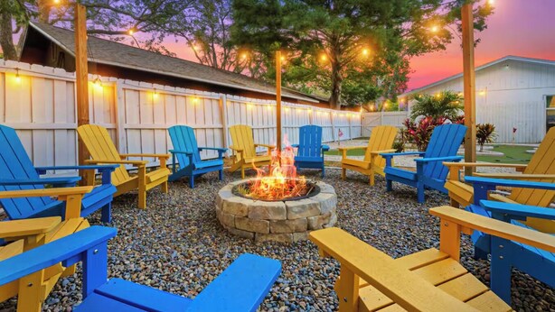 Eine Terrasse mit Adirondack-Stühlen, einem Steinkamin und Lichterketten.