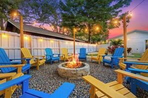A patio area with Adirondack chairs, a stone fire pit, and string lights.