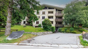 A multi-story building with balconies, surrounded by greenery and a stone wall. - Apartment Erica Bormio (Bormio)