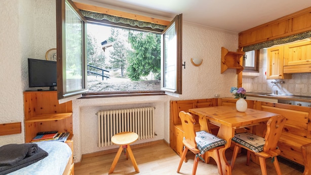 A compact kitchen with wooden cabinets, a dining table, and a window overlooking a garden. - Apartment Erica Bormio (Bormio)