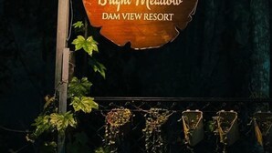 Une enseigne en bois indiquant l’emplacement du complexe hôtelier Bright Meadow Dam View, avec un logo et le nom du complexe.