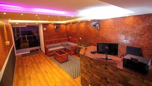 Un intérieur moderne avec un plancher en bois, un coin salon comprenant un canapé et une table basse, un comptoir d’accueil avec un ordinateur, et un mur à texture.