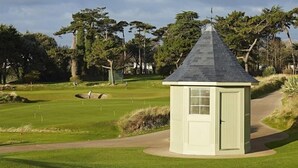 A small, light-colored structure with a peaked roof, situated on a golf course with a clear path leading to it. - Portmarnock Hotel And Golf Links (Portmarnock)