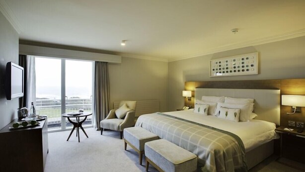 A hotel room with a large bed, a desk, a chair, a small table, and a television. - Portmarnock Hotel And Golf Links (Portmarnock)