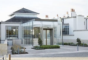 Stunning building with a glass facade, featuring a prominent entrance and a serene garden area with lush greenery and a seating area.