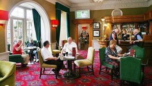 A hotel lobby with a bar area, seating arrangements, and a television screen. - Portmarnock Hotel And Golf Links (Portmarnock)