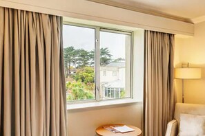 A hotel room with a large window, curtains, a round table with a book, and a lamp. - Portmarnock Hotel And Golf Links (Portmarnock)