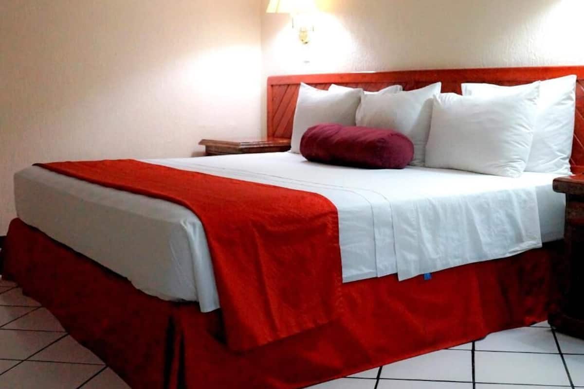 A hotel room with a bed, a nightstand, a lamp, and a red and white bedspread.