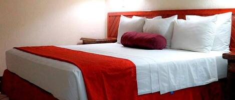 Una habitación de hotel con cama, mesita de noche, lámpara y colcha roja y blanca.