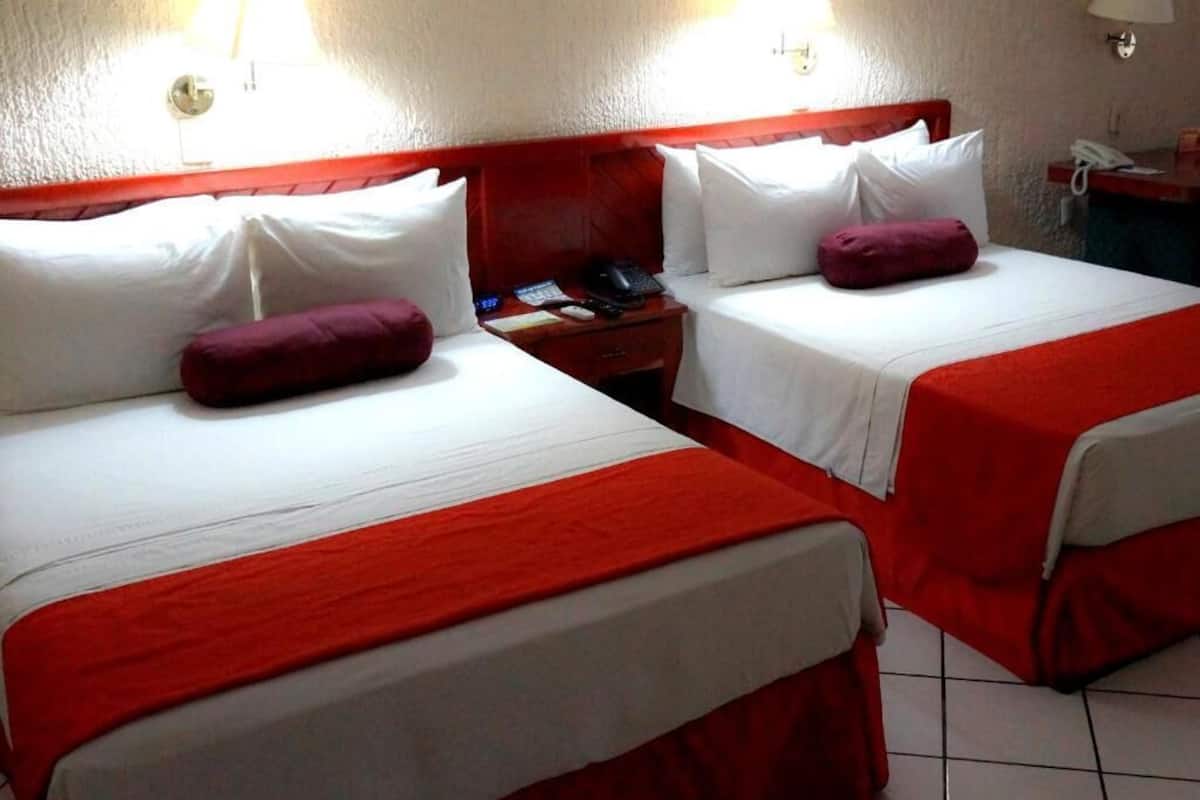 A hotel room with two beds, each with white bedding and red accents. There are two bedside tables with lamps and a phone.
