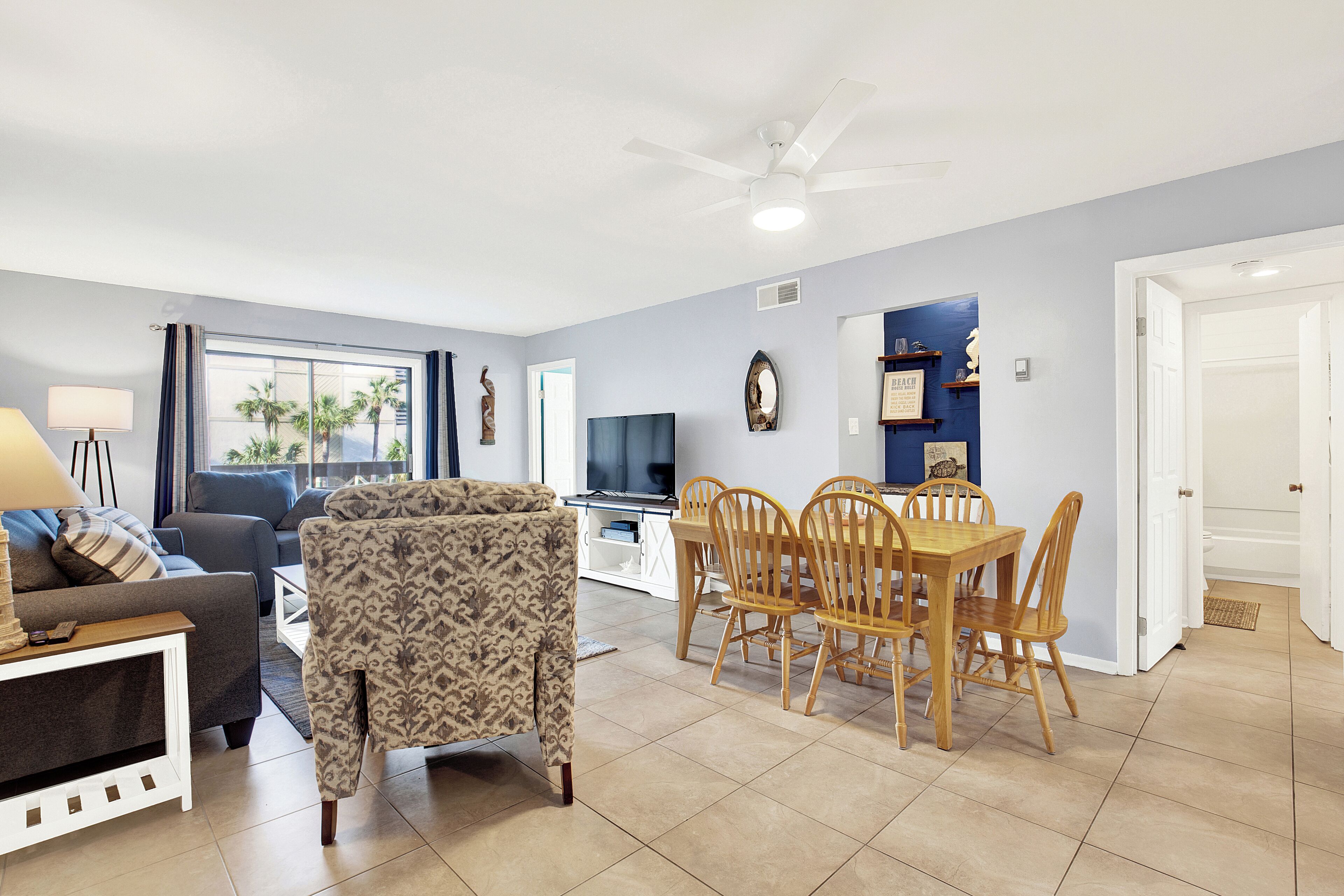 Una sala de estar con sofá, sillón estampado, mesa de comedor con sillas y televisor.