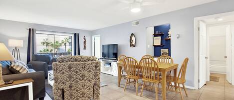Una sala de estar con sofá, sillón estampado, mesa de comedor con sillas y televisor.