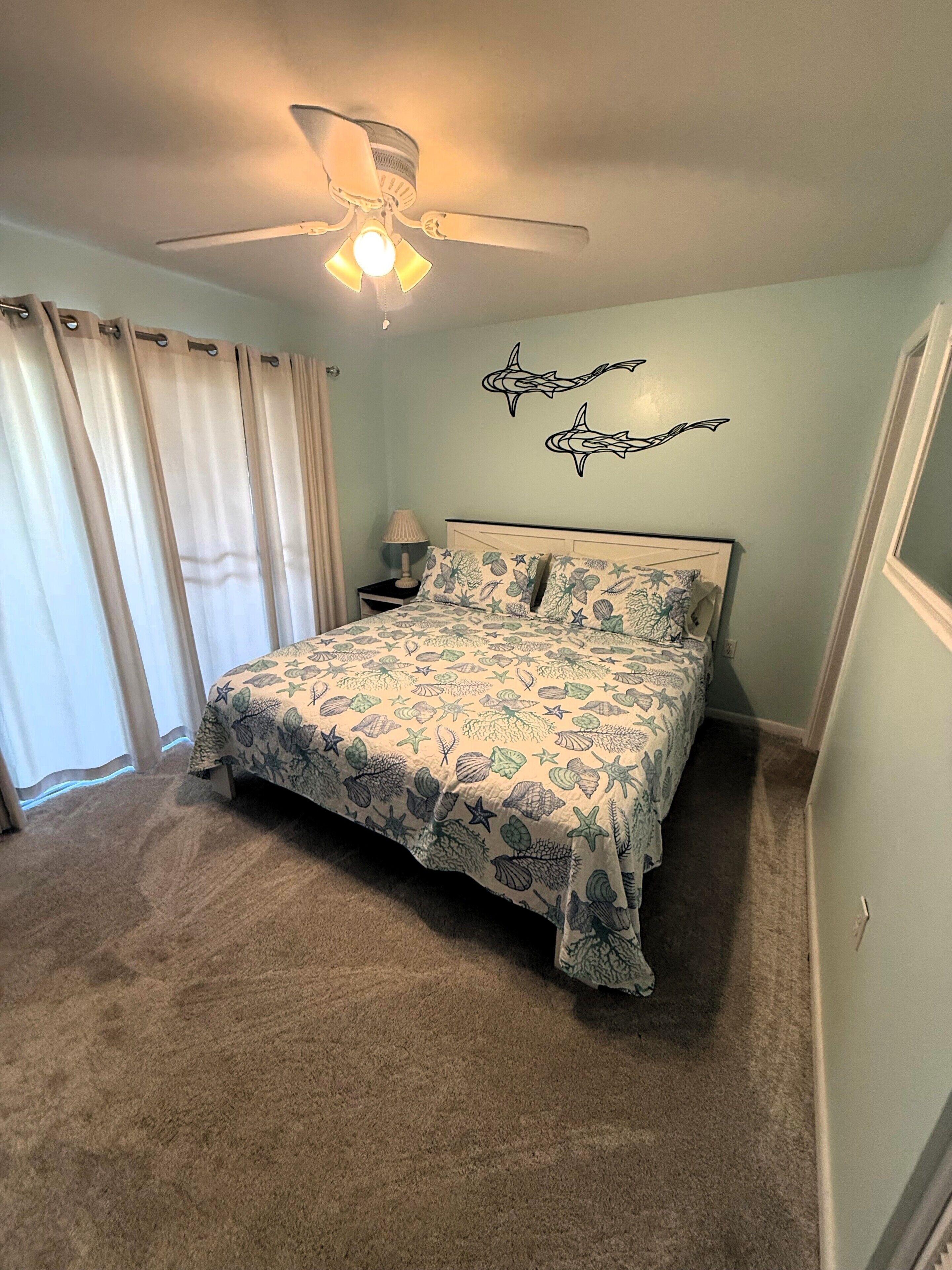 Une chambre à coucher avec un lit, un ventilateur de plafond et un mur décoré d’autocollants représentant des requins.