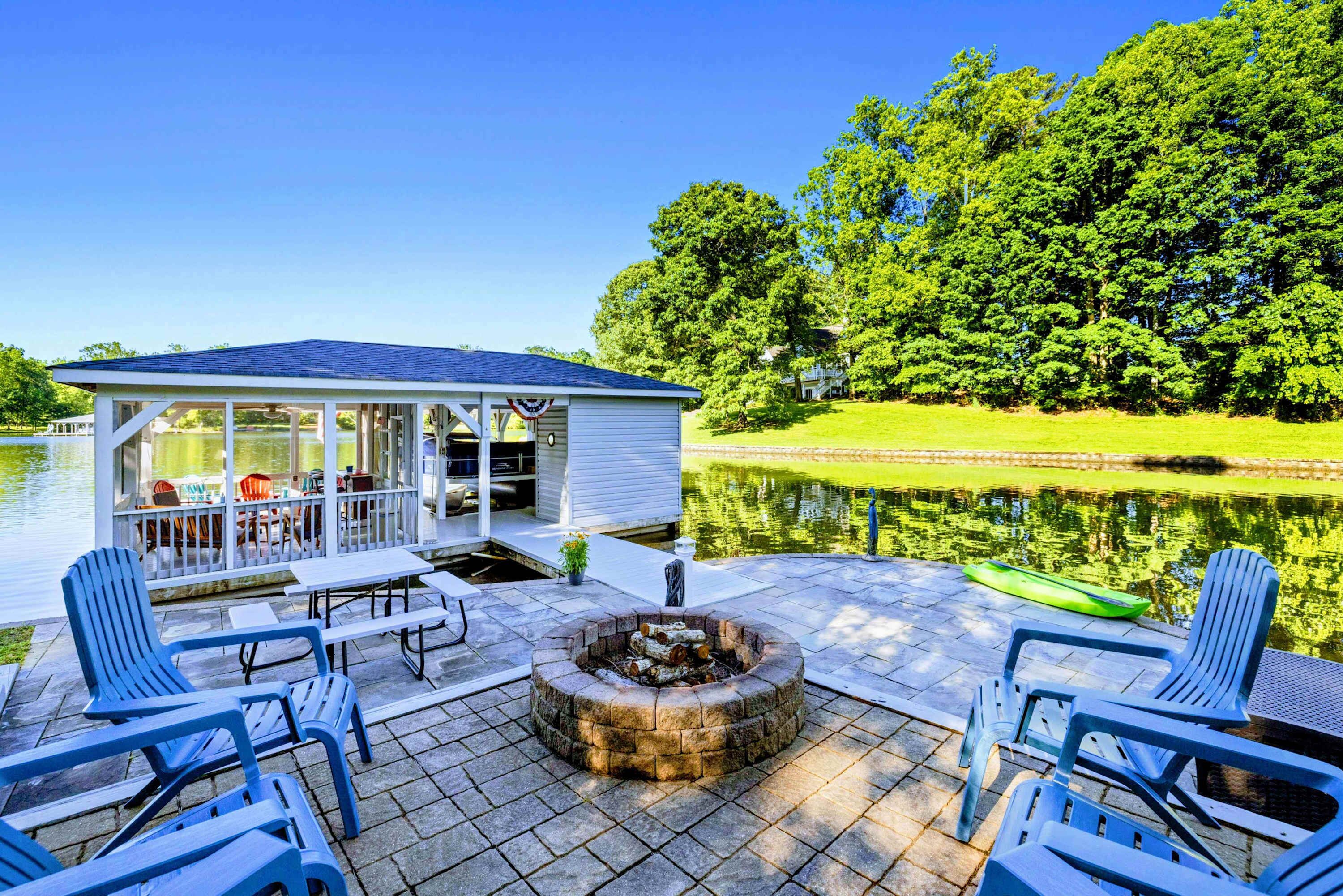 Un patio techado con mobiliario exterior, una chimenea y vistas a un lago.