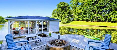 Un patio techado con mobiliario exterior, una chimenea y vistas a un lago.