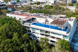 A modern hotel with a rooftop pool, multiple balconies, and a lush green environment. - 2 BR Condo with Rooftop Pool - Terrazas (Playa del Carmen)