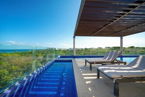 A rooftop infinity pool with lounge chairs, a glass balustrade, and a clear view of the ocean. - 2 BR Condo with Rooftop Pool - Terrazas (Playa del Carmen)