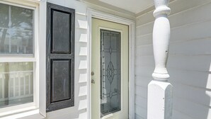 Una casa blanca con una puerta marrón oscuro y una ventana con contraventanas.
