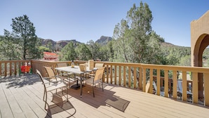 Eine Holzdar Terrasse mit Gartenmöbeln, darunter ein Tisch und Stühle, mit Blick auf eine gebirgige Landschaft.