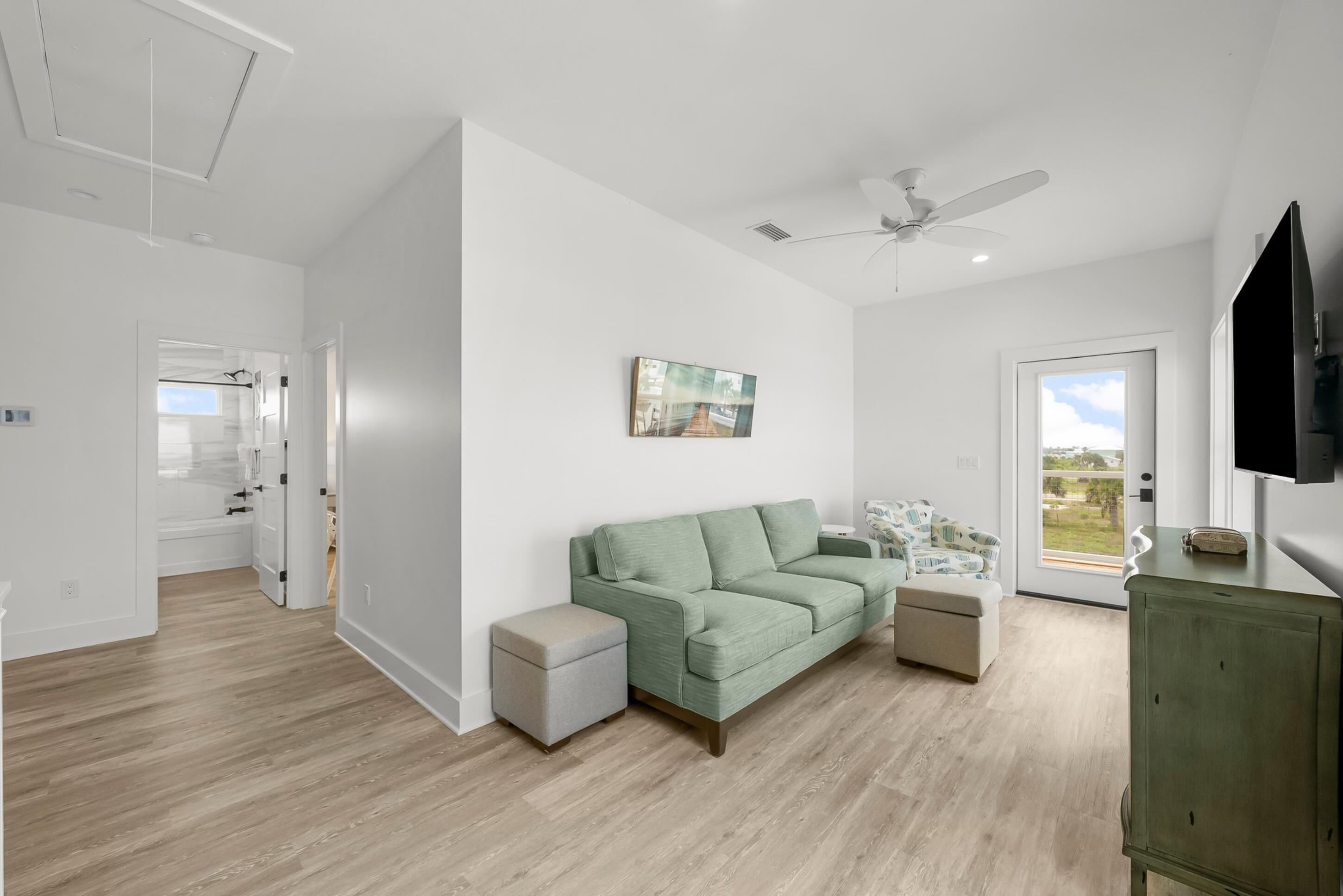 A spacious living room with a green sofa, a small side table, and a ceiling fan.