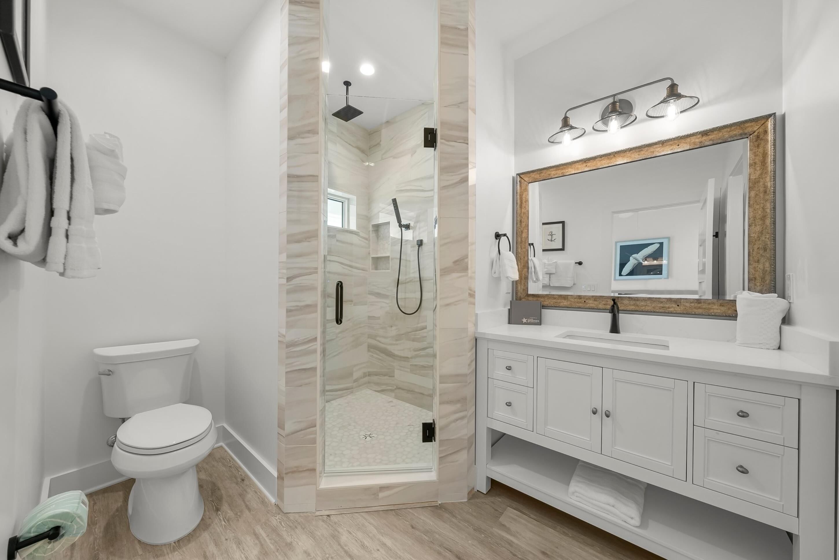 Une salle de bain moderne avec une douche à parois de verre, des toilettes blanches et un meuble-lavabo doté d’un grand miroir et d’un éclairage.