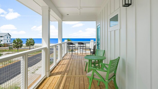 A wooden deck with a view of the ocean, a table with chairs, and a window with a view. - Beach House - Even Keel by PHG (Mexico Beach)