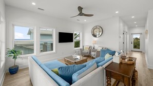 A modern living room with a sectional sofa, a coffee table, and a television mounted on the wall. - Beach House - Even Keel by PHG (Mexico Beach)