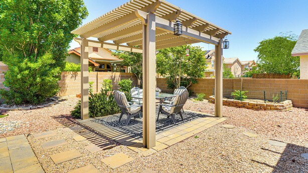 Un'area patio coperta con una pergola, posti a sedere all'aperto e un vialetto in ghiaia.
