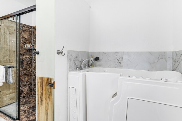 Ein modernes Badezimmer mit Duschkabine aus Glas, einer weißen Badewanne und einer Wand mit Marmorfliesen.