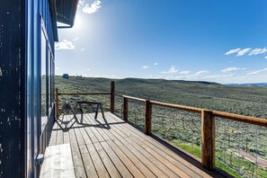 Eine Holzterrasse mit Metallgeländer, das auf eine hügelige Landschaft blickt.
