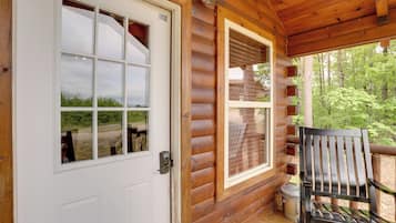 Una cabaña de madera con puerta y ventanas blancas, un banco en el exterior y vistas del bosque circundante.