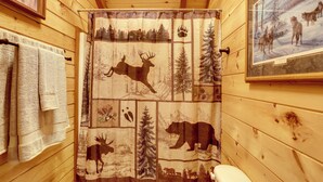 Ein Badezimmer einer Holzdiele mit Duschvorhang mit Tierdrucken, einer Toilette und einem gerahmten Bild an der Wand.