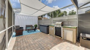 Une terrasse extérieure couverte, dotée d’un sol carrelé à motifs hexagonaux, d’un barbecue et d’un espace détente avec une table et des chaises.