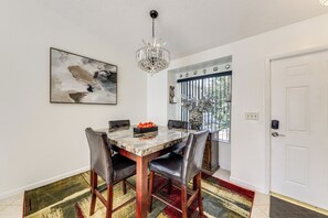 Un coin repas avec une table en marbre, des chaises en cuir, un lustre, un tableau abstrait encadré et une vue par une fenêtre munie de stores.