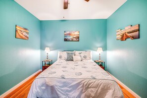Ein Schlafzimmer mit türkisfarbenen Wänden, einem Bett mit einem weiß-blauen Bettbezug im Meeresstil, zwei Nachttischen mit Lampen und drei gerahmten Bildern an den Wänden.