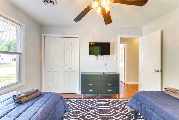Une chambre avec deux lits, un ventilateur de plafond, une télévision et une commode.