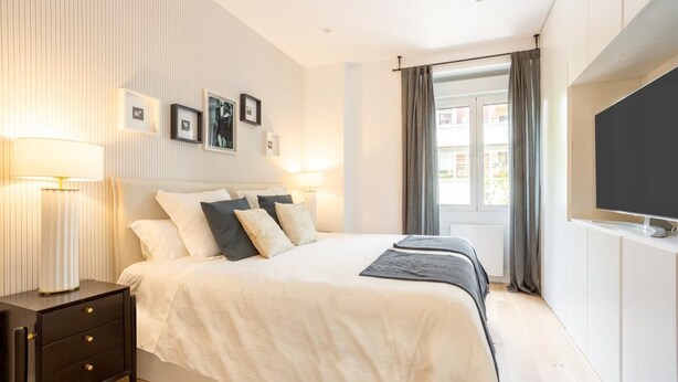A modern bedroom with a large bed, bedside lamps, a flat-screen TV, and a window with curtains. - Luxury in downtown Madrid. (Madrid)