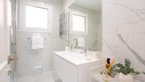 A modern bathroom with a large mirror, white marble walls, a glass shower enclosure, and a vanity with a white countertop. - Luxury in downtown Madrid. (Madrid)