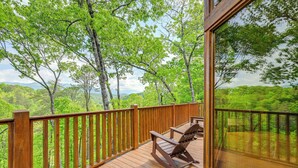 A wooden deck with a rocking chair, overlooking a lush green landscape with trees and distant mountains. - Game Room, Hot Tub & Decks: Scenic Franklin Cabin (Franklin)