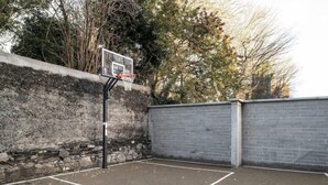 An outdoor basketball court with a hoop, surrounded by stone walls and a brick wall. - Arran Quay - Ardcairn House - Campus Accommodation (Dublin)