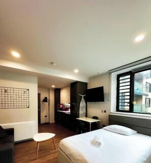 A modern hotel room with a bed, a desk, a chair, a TV, and a window. - Arran Quay - Ardcairn House - Campus Accommodation (Dublin)