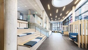 A spacious indoor area with a staircase, seating areas, and a high ceiling with linear lighting. - Arran Quay - Ardcairn House - Campus Accommodation (Dublin)