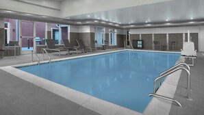 Una piscina interior con agua cristalina, rodeada de sillones de descanso y un suelo de baldosas.