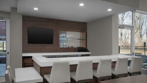 Una cocina moderna con barra, taburetes blancos y un ventanal con vistas a árboles.