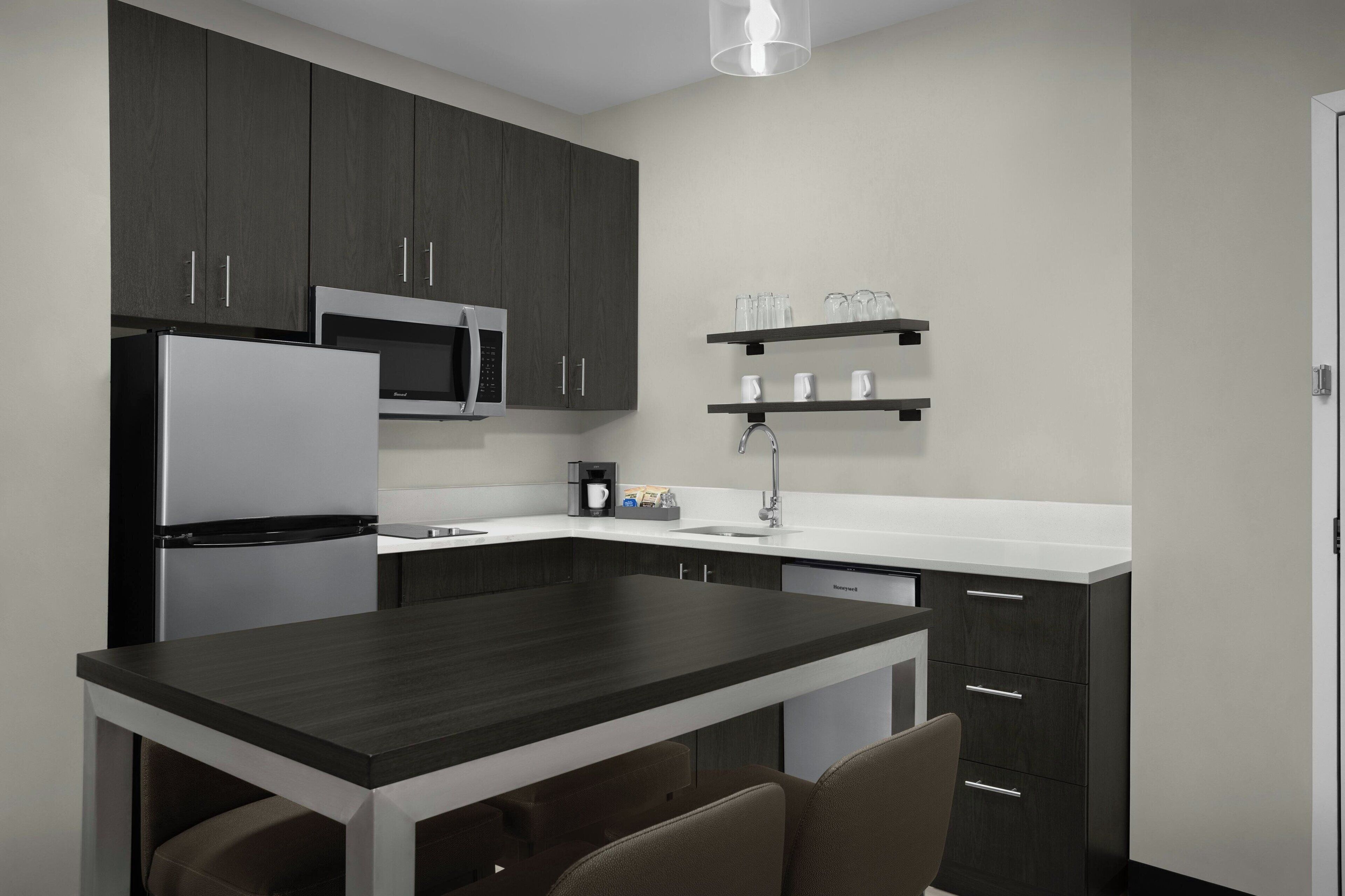 A modern kitchen with dark cabinets, a white countertop, a built-in microwave, a coffee maker, and a dishwasher.