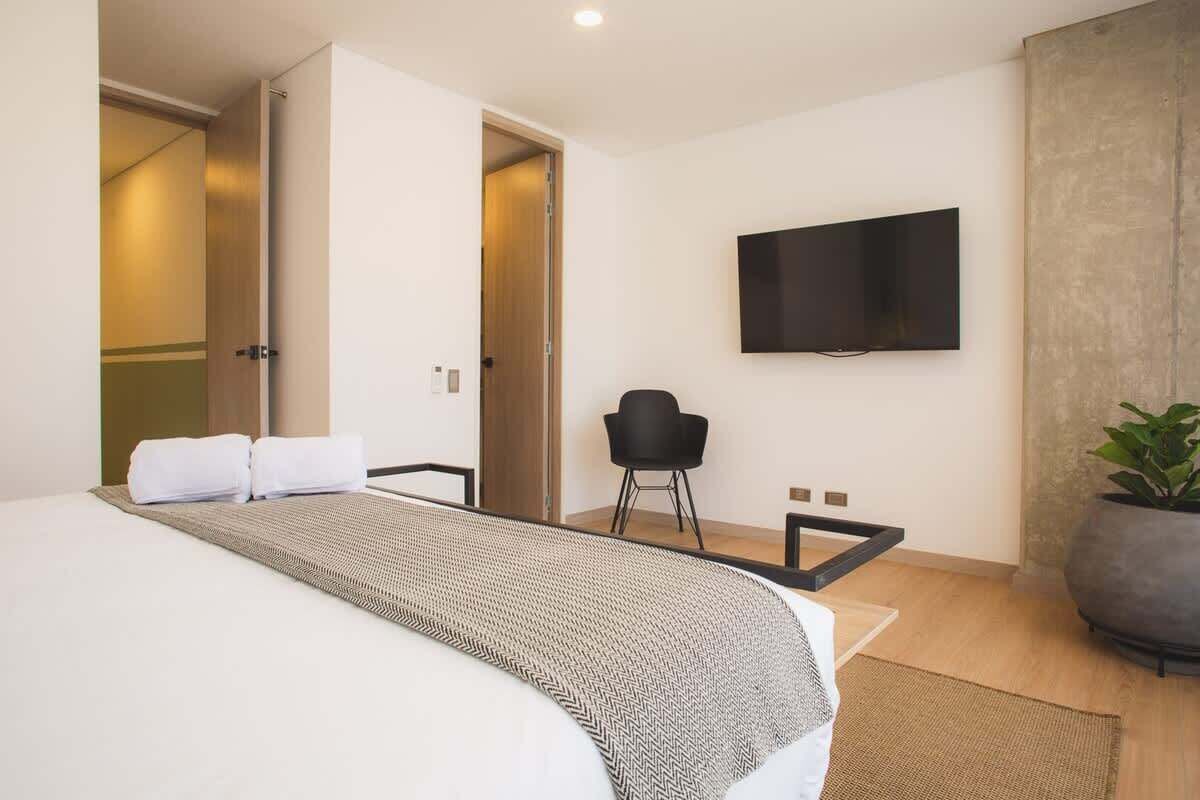 Et moderne hotelværelse med en stor seng, et fladskærms-tv på væggen, en sort stol og en potteplante.