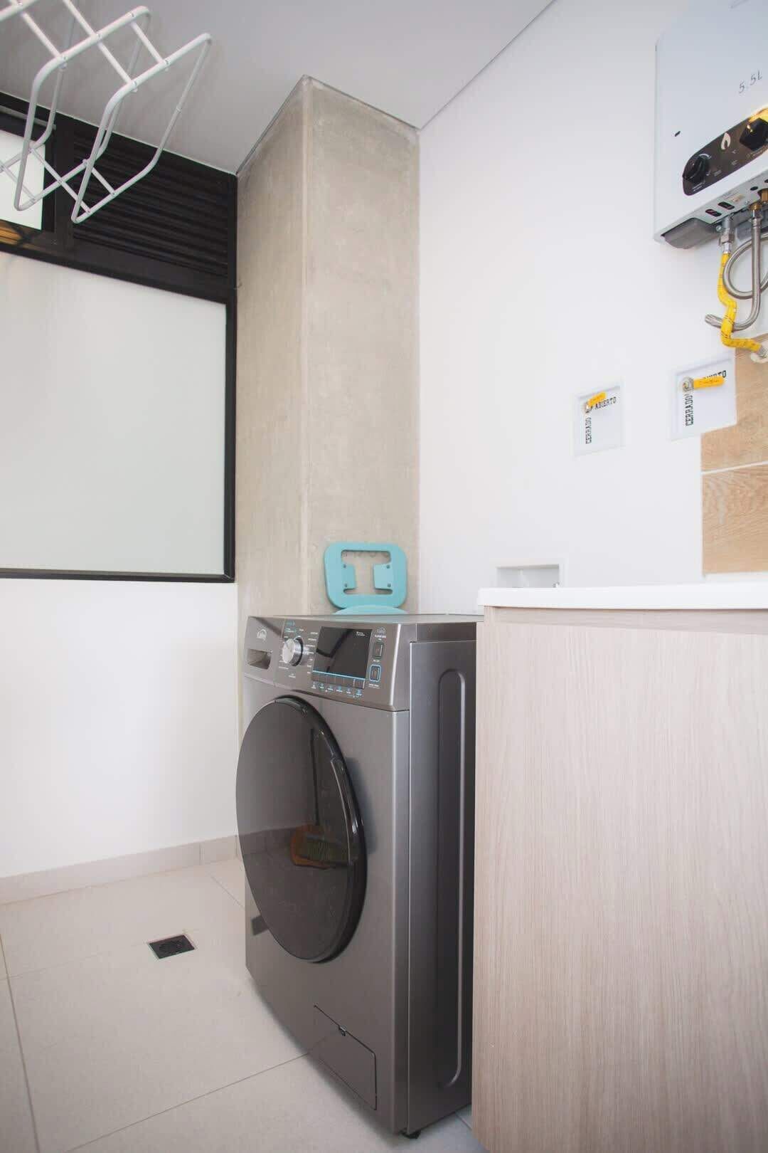 A compact laundry room with a washing machine, a drying rack, and a small countertop.