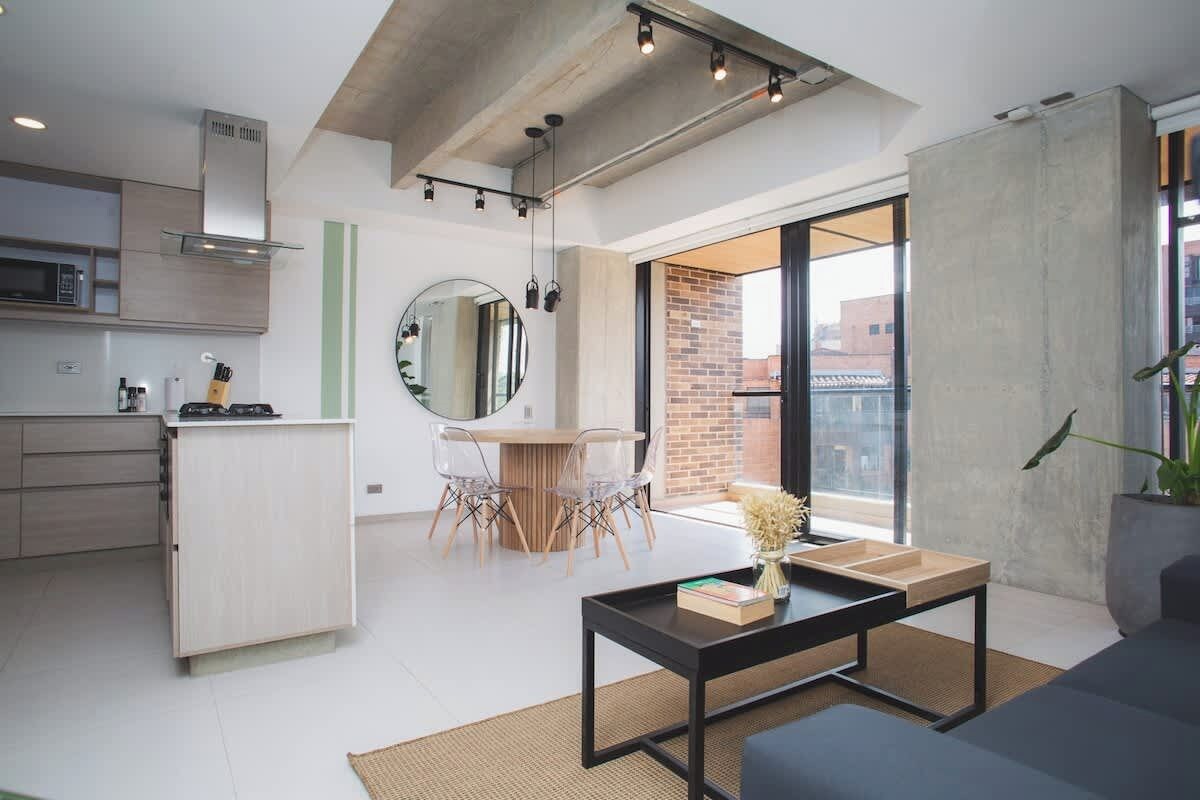 Een moderne keuken met een magnetron, een houten kast en een eethoek met een ronde spiegel en transparante stoelen.