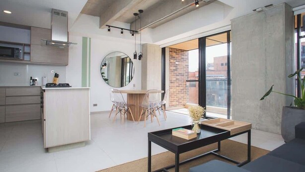 A modern kitchen with a microwave, a wooden cabinet, and a dining area with a round mirror and clear chairs. - Cool 3 BR W/ Balcony in Laureles Medellín (Medellín)