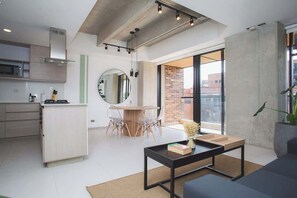 A modern kitchen with a microwave, a wooden cabinet, and a dining area with a round mirror and clear chairs. - Cool 3 BR W/ Balcony in Laureles Medellín (Medellín)